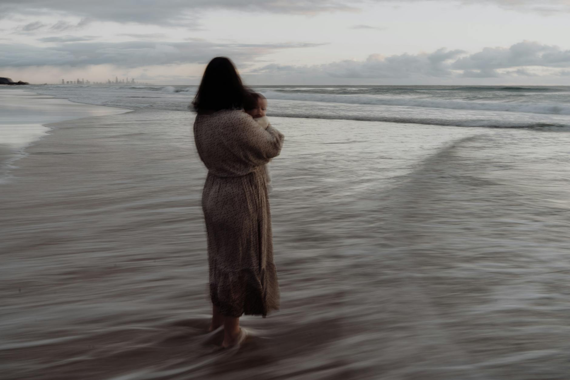 woman with baby in arms stands in sea